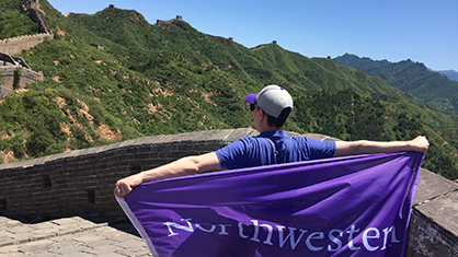 A Northwestern staff member holds a Northwestern flag up on the Great Wall of China