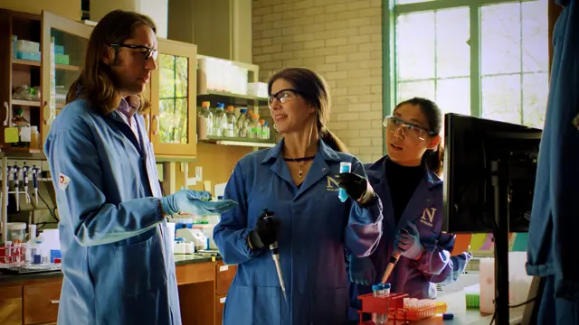 three students in lab coats conversing