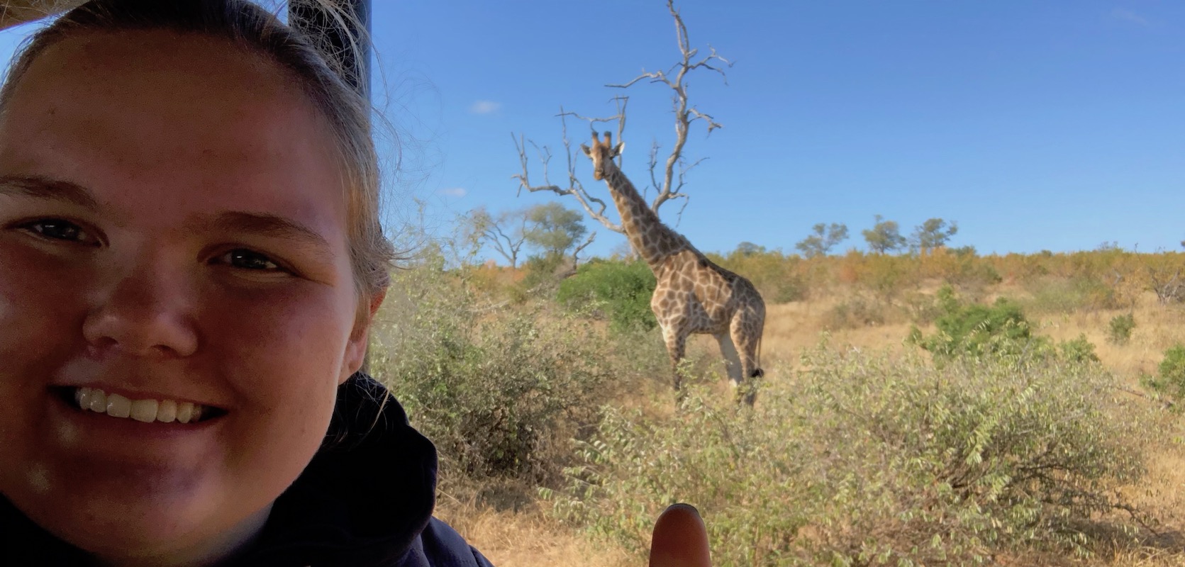 Student on safari with giraffe in the distance 