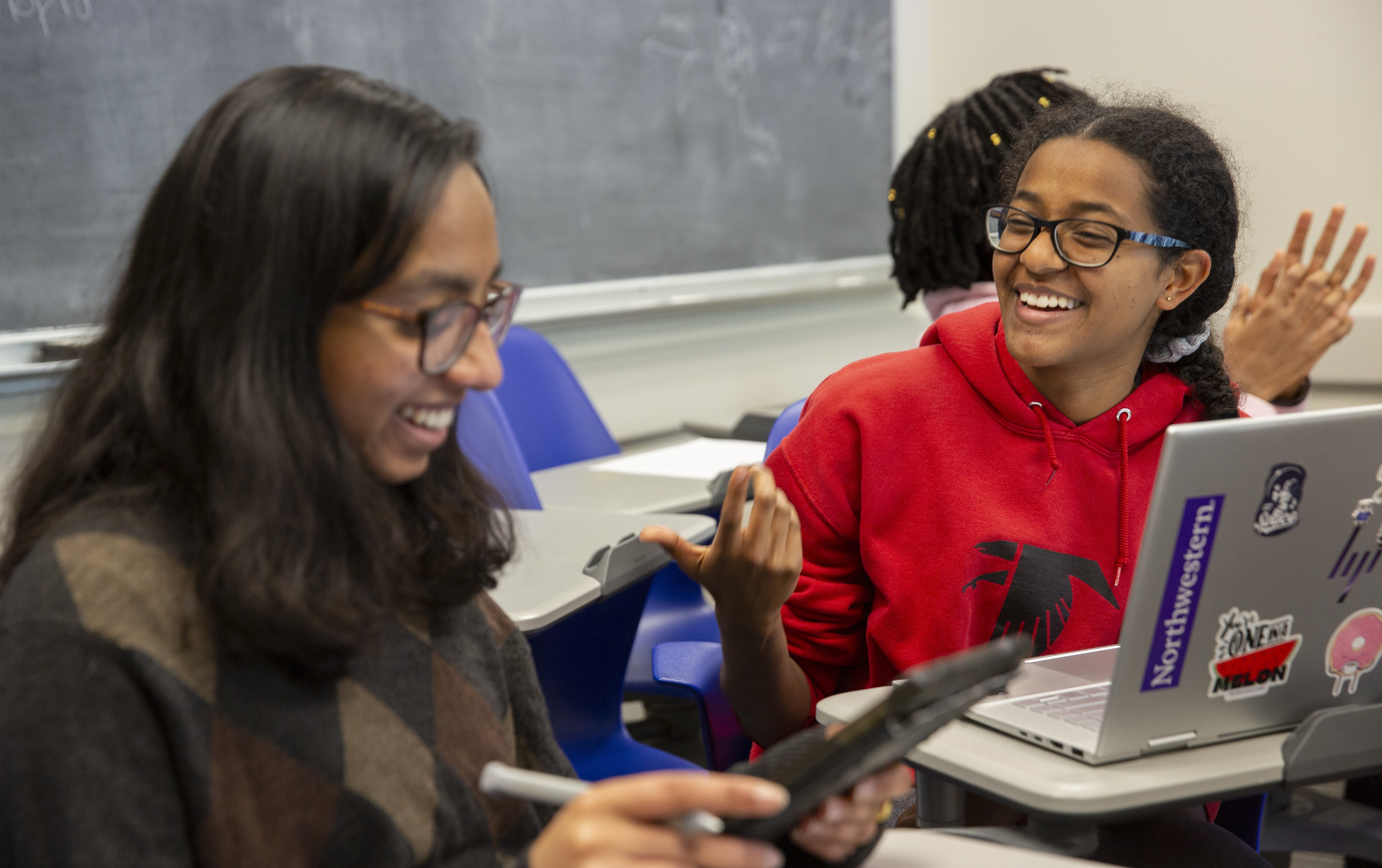 Two student seated in classroom, talking and smiling