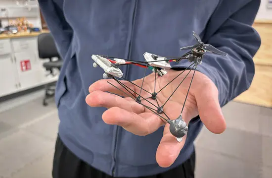 Hand holding a tiny custom drone prototype in a lab.