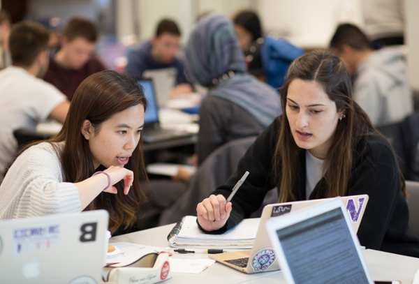 two students talking at table looking at a laptop screen