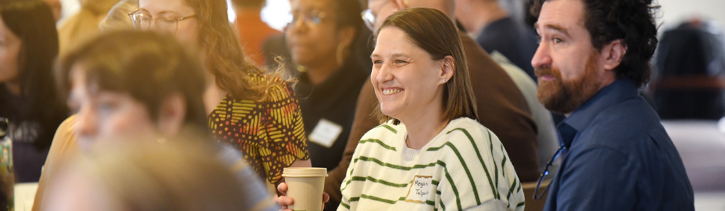 A woman smiling at a table with others at catalystNU first full day session