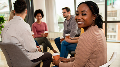 Group of 5 people sitting in circle, a Black person is turned towards the camera.