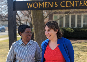 Photo of Njoki Kamau (left) and Sarah Brown (right) standing outside in front of a sign that says "Women's Center"