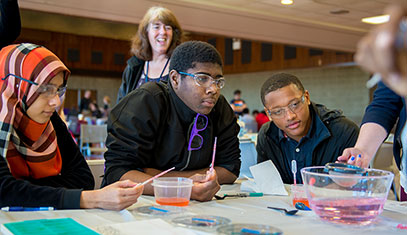 students sitting around a table, watching a chemistry demonstration