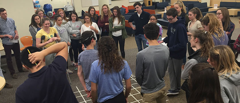 Students looking at a grid made of tape on the floor.