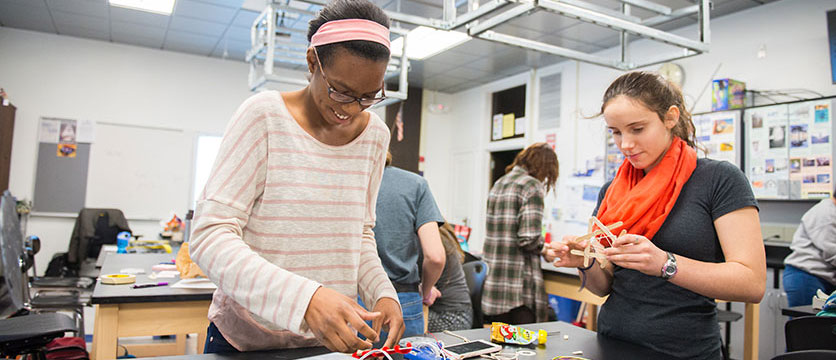 Image of two girls making things out of pipe cleaners, wires and popsicle sticks.