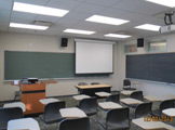 View of classroom seats, podium, and screen at front of room.