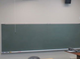 View of blackboard, podium and wall-mounted speakers.