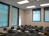 View of classroom seating, windows, florescent lights and ceiling-mounted projector.