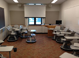 Pictures of chairs set up in a semi circle, gray with a desk attached to the arm.  You can also see a projector and the screen in the halfway down position