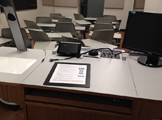Picture of the teacher's podium with monitor and overhead projector and computer cables the view is facing the class