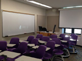 Picture of the room facing the window with purple chairs and whiteboard