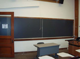 View of podium, blackboard, and classroom door.