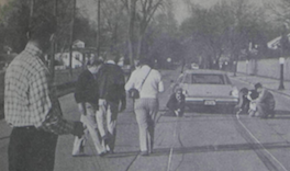 old photo of people walking on the street with car parked on side