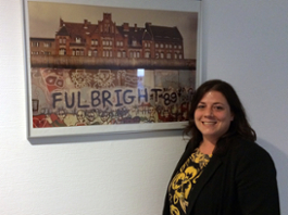 Catrina DeBord standing in front of a picture showing "Fulbright 89" graffitied on the Berlin Wall