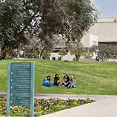view of a campus with building in background and 4 students sitting on gras