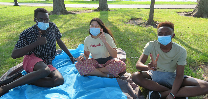 students outside by the lake sitting in the grass and wearing facemasks
