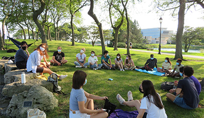 students-wearing-masks-while-sitting-in-the-grass-outside-on-campus