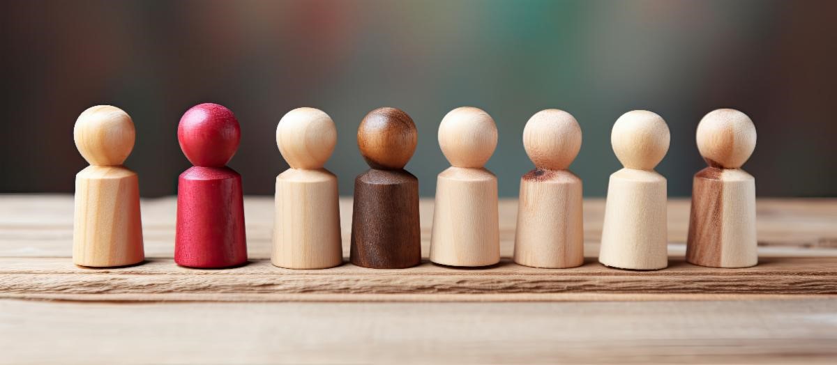 Seven wooden figurines of varying colors, including one red, arranged in a line on a wooden surface.