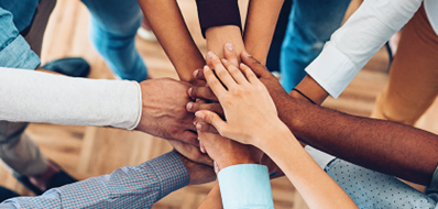 Hands of diverse individuals joined together over a wooden floor.