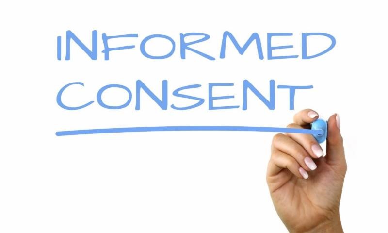 Hand holding a blue pen, writing informed consent on a white paper