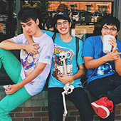 three teenage boys sitting on a brick wall outside a store