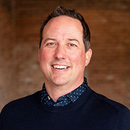 man with dark brown hair and blue shirt with polka dots smiling