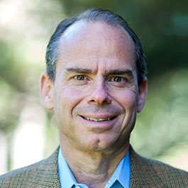 man with dark gray hair and brown checkered suit smiling
