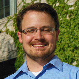 man with brown hair and beard with glasses and blue shirt smiling