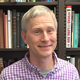 man with white hair and purple checkered shirt smiling