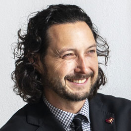 smiling man in suit with dark hair, mustache, beard