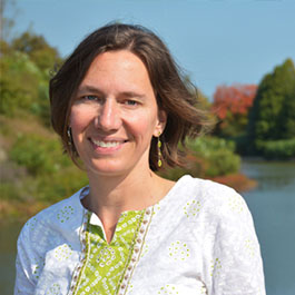 woman with short brown hair with green earrings smiling