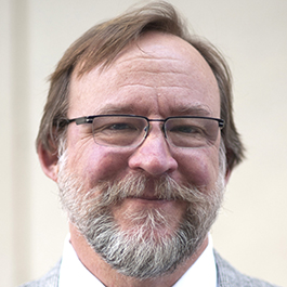 man with brown hair and white beard and glasses smiling