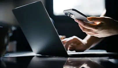 perdon typing on laptop and holding the phone