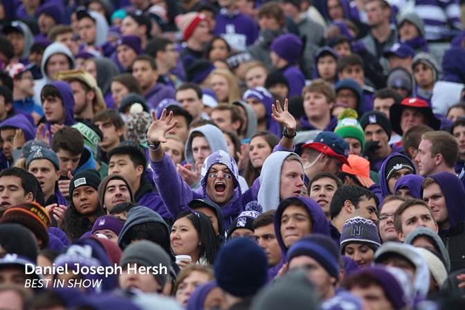 A picture of a bunch of students at a football game with one student facing the camera holding a claw