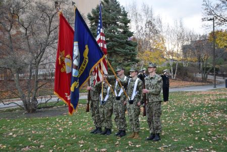 Five students in military uniforms stand at attention during a Veterans Day service.