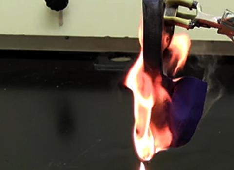 Piece of lab coat on fire held by tongs