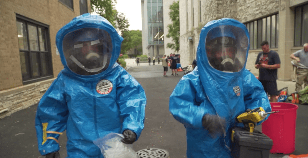 Two hazmat workers in protective suits near Tech building