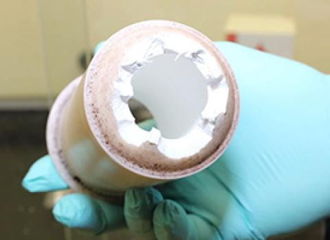 Gloved hand holding a damaged pressure vessel