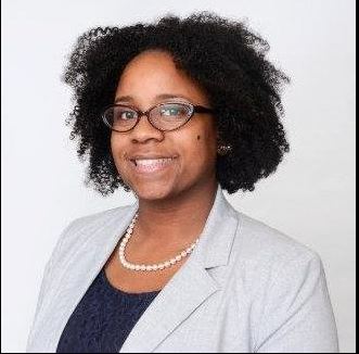 photo of devin moran, SJE director. she is a Black woman in a green shirt with glasses and braids.
