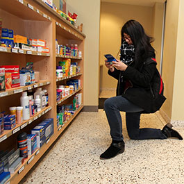 girl kneels in front of medicine shelf