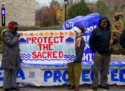 Two students hold a banner that says "Protect the Sacred"