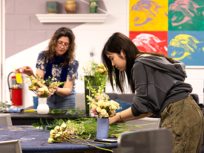  A student creates a floral arrangement while her instructor shows techniques in the background