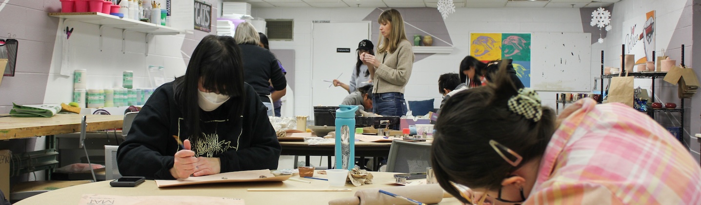 students paint ceramics in a studio while a teacher talks in the background