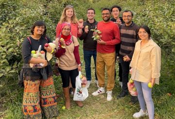 8 members of the Goyal lab smiling in an apple orchard