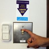 A hand turns off a light switch under a sign reading "lights out"
