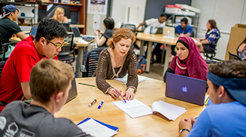 Students sitting around a table with an instructor showing them information.