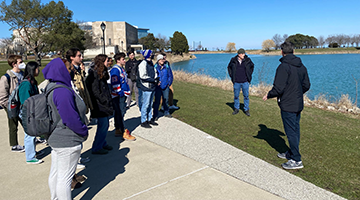 Students standing outside near water listening to an instructor give a tour.